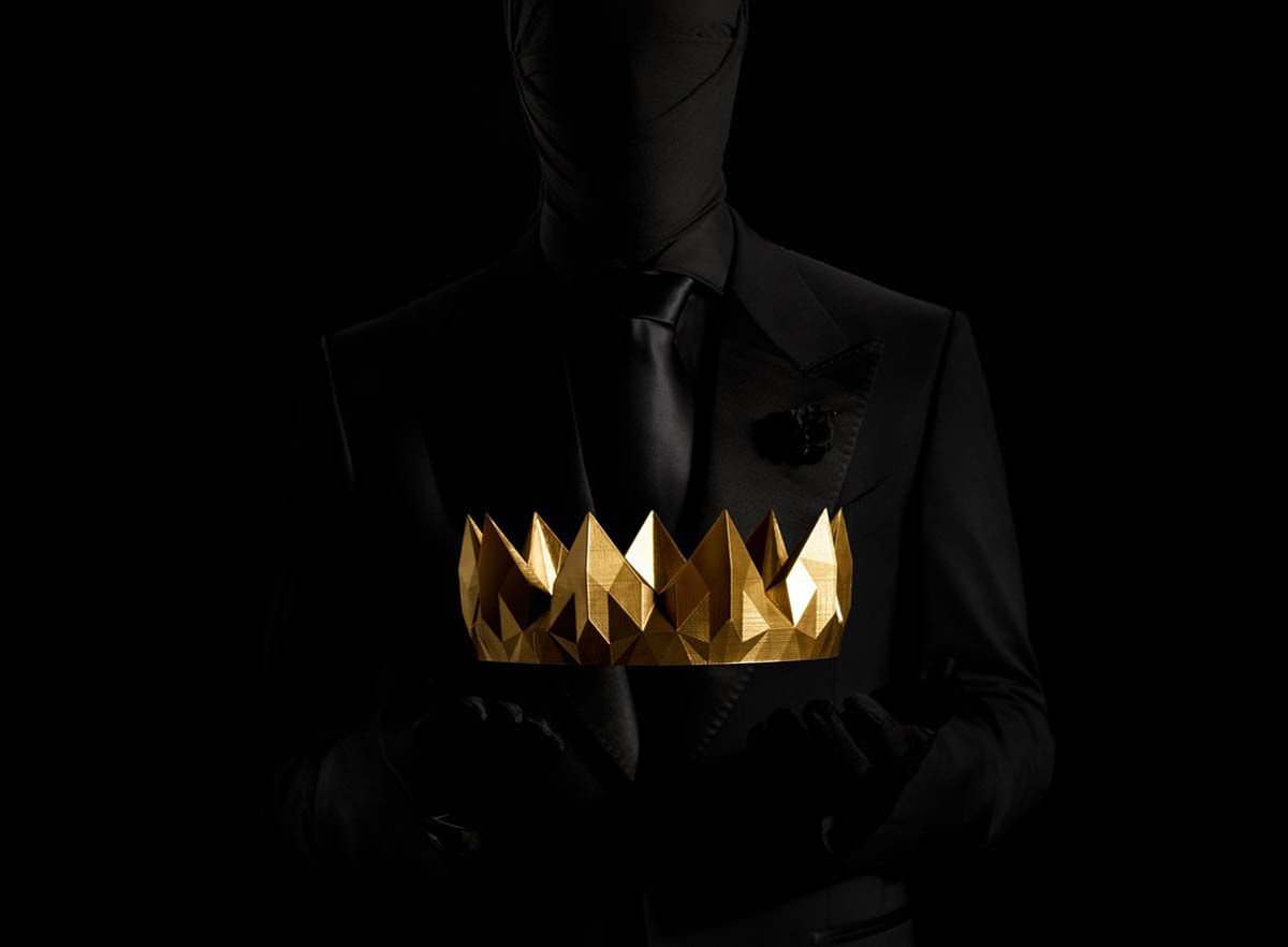 Dark image of a man in a suit about to accept a golden crown