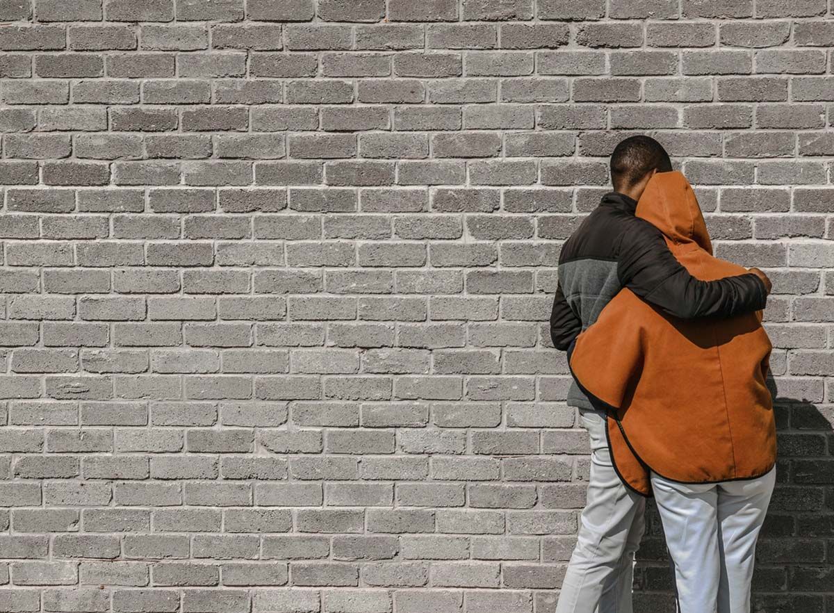Couple with arms around each other facing a wall